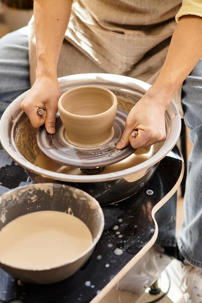 Hands sculpt a clay pot on a wheel, surrounded by tools and materials in a bright pottery studio.