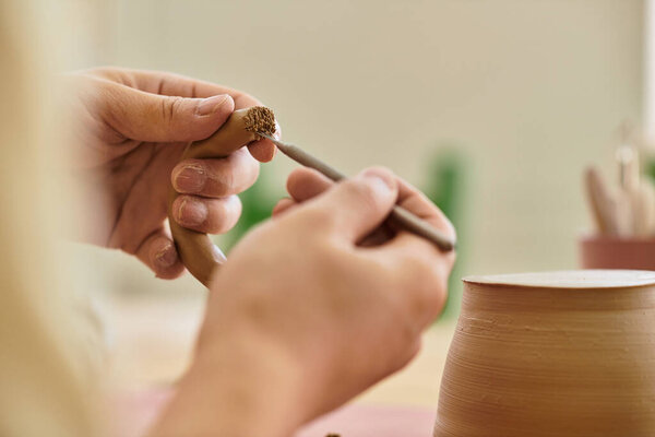 Hands shape and refine a clay piece, showcasing creativity in a well lit pottery studio.