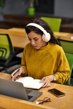 Modern bir ofiste, sarı kazaklı genç bir kadın notlar yazmaya odaklanır..