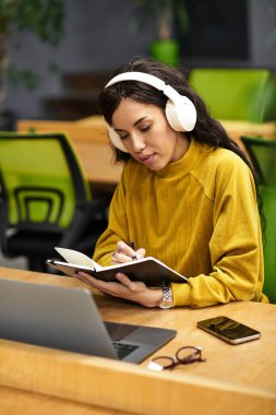 Canlı bir ofiste, zarif genç bir kadın notalarına odaklanırken müzik dinler..