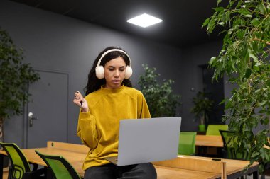 Sarı kazaklı güzel bir kadın şık bir ofis ortamında laptopunun başında çalışıyor..