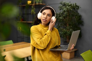 Şık giyinmiş genç bir kadın, ofiste müzik dinlerken dizüstü bilgisayarında çalışıyor..