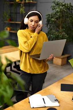 Kulaklık takan genç bir profesyonel şık bir ofiste dizüstü bilgisayarda çalışıyor..