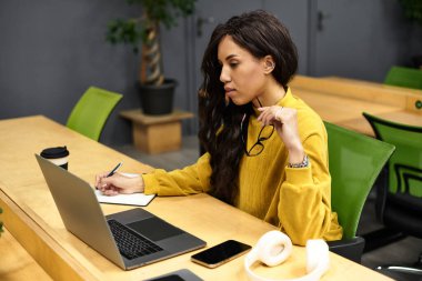Güzel genç bir kadın şık bir ofis masasında oturmuş notlar yazarken işine odaklanıyor..
