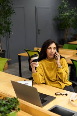 Profesyonel kadın masasında oturuyor, kahve içiyor ve mesai saatlerinde telefonla konuşuyor..