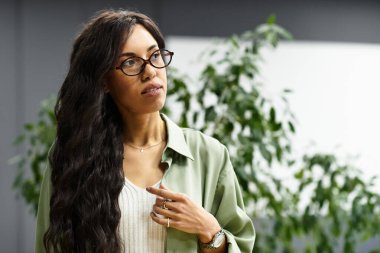 Şık bir ofis ortamındaki güzel kadın yeşilliklerle çevriliyken fikirlerini ifade ediyor..