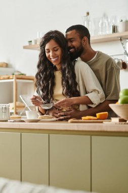 Bir çift, sıcak bir mutfakta yemek hazırlarken sevimli bir gülümsemeyi paylaşıyor..