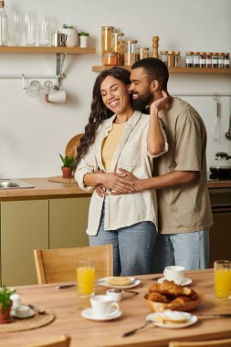 Neşeli bir çift evlerinin mutfağında kucaklaşıyor, kahvaltıda gülüşlerini ve sevgilerini paylaşıyor..