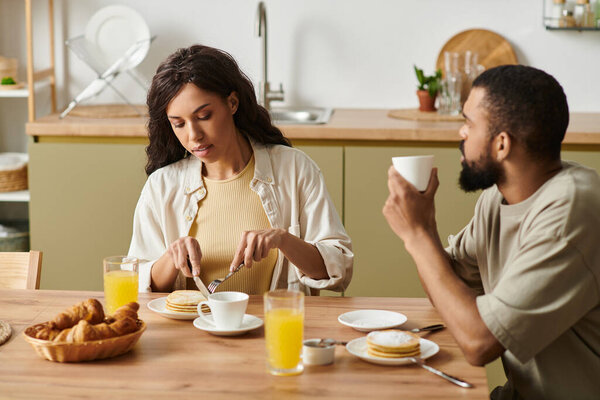 The couple enjoys a cozy breakfast at home with pancakes and drinks.