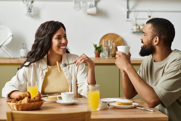 Пара наслаждается уютным завтраком дома, смеясь и делясь сладкими моментами во время еды.