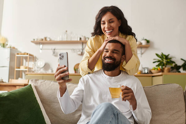 A joyful African American couple takes a selfie, sharing laughter in their cozy living room.