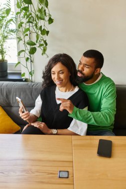 Afro-Amerikalı bir çift bir kafedeki telefona bakarken gülümsüyor..