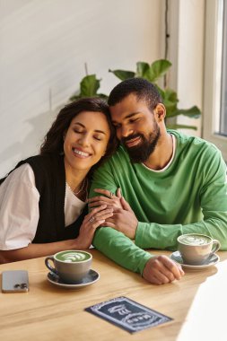 Afro-Amerikalı bir çift, rahat bir kafede içki içerken gülümsüyor..