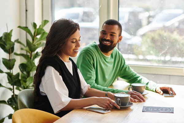Афроамериканская пара делится смехом и кофе в кафе в солнечный день.