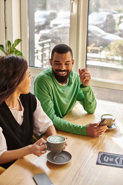 Счастливая афроамериканская пара наслаждается теплыми напитками вместе в причудливой обстановке кафе.