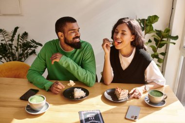 İki birey, huzurlu bir kafede gülüşlerini ve lezzetli yemeklerini paylaşıyor, birlikte vakit geçiriyorlar..