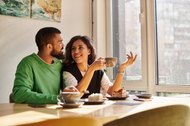 Sıcak, davetkar bir kafede kahve içerken gülüp sohbet eden bir çift..