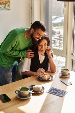 Afro-Amerikalı bir çift sıcak bir kafe ortamında tatlı ikramlardan ve kahkahalardan hoşlanır..