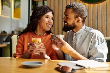 Afro-Amerikalı bir çift sıcak bir kafe ortamında kahkaha ve içki paylaşıyor, neşe saçıyor..