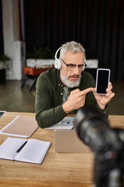 Çalışma alanındaki odaklanmış bir birey, kulaklık takarken akıllı telefon detaylarını açıklar.