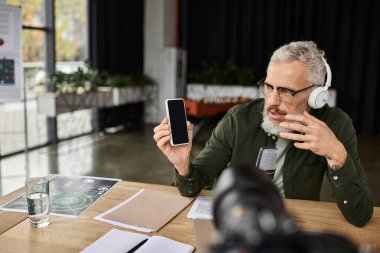 Profesyonel bir adam, çağdaş bir ortamda akıllı telefon sergilerken sanal bir tartışma yürütüyor.