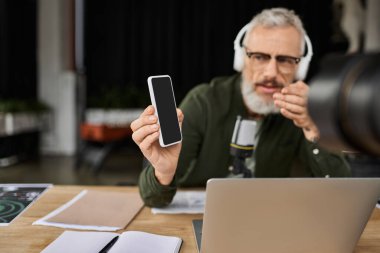 Modayı takip eden bir ofiste çalışan kişi, akıllı telefonu gösterirken ve mikrofon kullanırken tutkuyla konuşur.