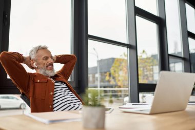 Profesyonel kulaklıklı, geniş pencereli şık bir masada gülümsüyor..