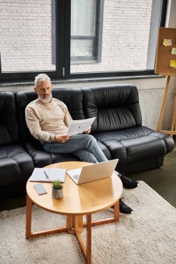 Bir adam şık bir ofiste rahatça kitap okur, rahatlıkla verimliliği birleştirir..