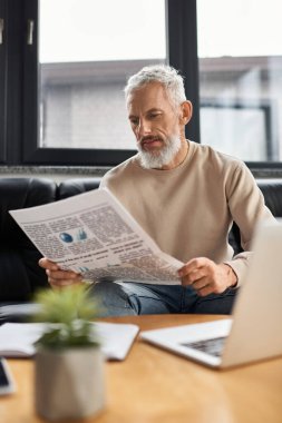 Yaşlı bir adam, modern bir ofiste rahat bir şekilde otururken sabah gazetesinden zevk alır..