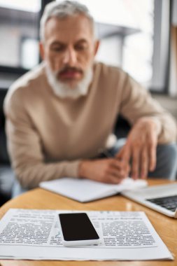Bilgisayarla çevrili akıllı telefon ve notlarla dolu kağıtları dikkatle inceleyen kişi.