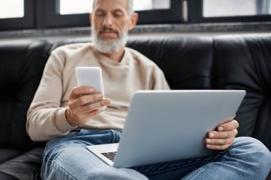 Bir kişi, şık bir çalışma alanında görevlere daldırılmış bir dizüstü bilgisayar ve akıllı telefon kullanır..