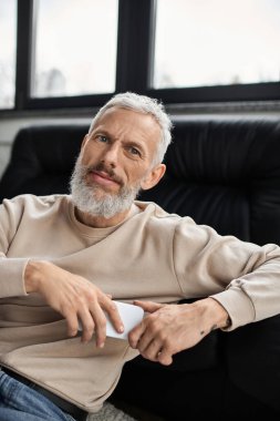 Sakallı rahat bir adam modern bir ofiste rahatça oturup içeceğinin tadını çıkarıyor..