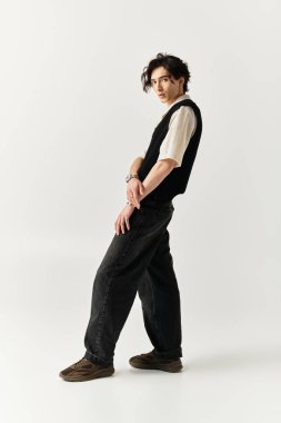 Kendine güvenen genç bir adam, minimalist bir stüdyoda modaya uygun bir kıyafet sergiliyor..