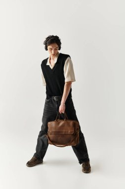 Yakışıklı genç adam şık bir çanta tutarken kendine güvenen bir şekilde poz veriyor..