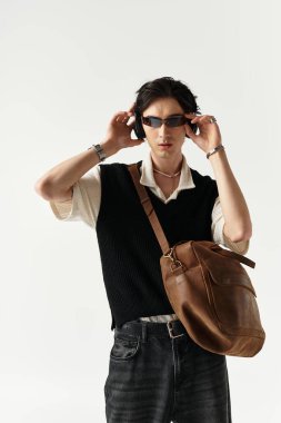 Moda kıyafeti giyen yakışıklı genç bir adam, iyi ışıklandırılmış bir stüdyoda güven içinde poz veriyor..