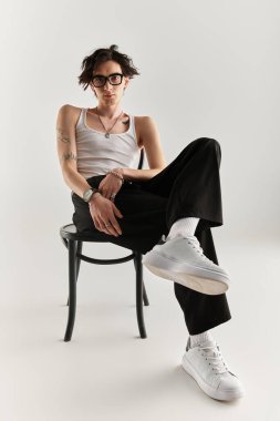 Zayıf genç bir adam, beyaz bir atlet ve modaya uygun bir kıyafetle kendinden emin bir şekilde poz veriyor..