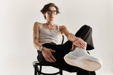 Beyaz kolsuz tişörtlü zayıf bir genç parlak bir stüdyoda kendine özgü bir stil sergiliyor..