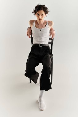 Genç bir adam, modaya uygun beyaz bir bluz ve parlak altlarıyla bir sandalyede otururken kendine güvenir..