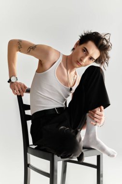 Parlak bir stüdyoda, kolsuz tişörtlü sıska bir genç kendine güvenen bir sandalyede poz verir..