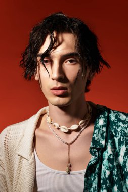 Sıska bir genç adam, renkli bir yaz kıyafeti içinde cesur bir arka plana karşı güvenle poz veriyor..