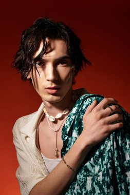 Genç bir adam canlı bir yaz kıyafeti içinde, moda anlayışını sergileyerek güven içinde poz verir..