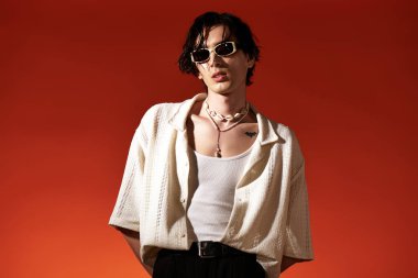 Genç adam, canlı turuncu bir arka plana karşı, modaya uygun bir yaz kıyafetiyle poz veriyor..