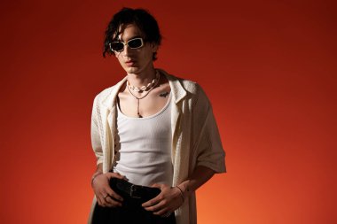 Genç adam kendine güvenerek poz veriyor, bir stüdyo ortamında şık bir yaz kıyafeti sergiliyor..