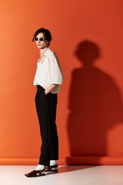 Genç bir adam canlı turuncu bir arka planda şık yaz kıyafetlerini sergiliyor..