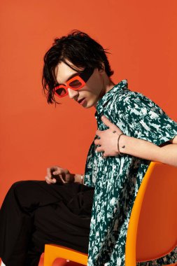 Şık bir genç adam yaz kıyafetleriyle göz alıcı turuncu bir arka plana karşı güvenle poz veriyor..