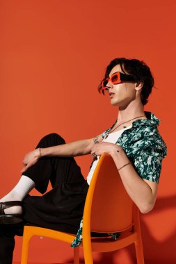 Sıska bir genç, bir stüdyoda otururken moda olan yaz modasını sergiliyor..