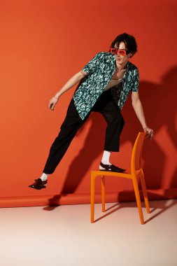Moda düşkünü genç adam turuncu bir zemine karşı yazın neşeli pozlar veriyor..