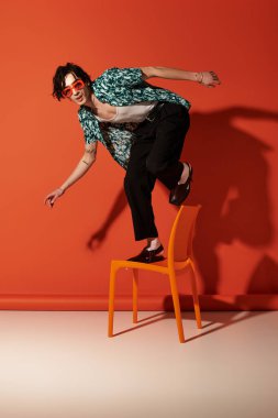 Sıska genç adam şık bir yaz kıyafetiyle gösteriş yapıyor. Sandalyede dengede duruyor..