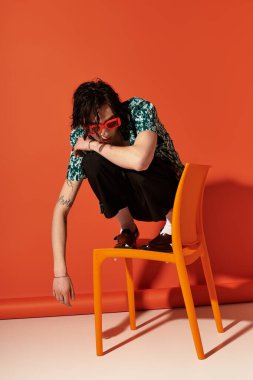 Genç adam yaz modasına uygun bir şekilde otururken turuncu bir arkaplan sergiliyor..