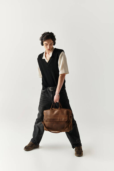 Красивый молодой человек уверенно позирует в шикарном наряде, держа стильную сумку.